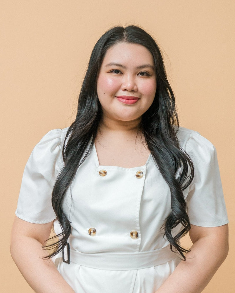 Christal Escandor wearing a white dress with gold buttons against a beige background